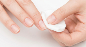 Woman cleaning fingernail with alcohol wipe to remove natural oils for long-lasting manicure