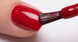 Close-up macro shot of nail polish brush capping the free edge of a fingernail with red polish to prevent chipping