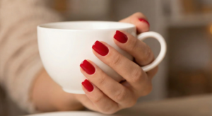 Woman holding a white coffee cup showcasing a glossy, chip-free red manicure that lasts up to two weeks