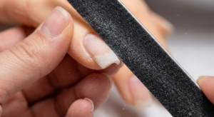 Action shot of filing the nail edge with a coarse board to create a square shape