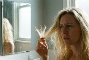 Woman looking in mirror examining damaged frizzy hair with split ends