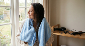 Woman gently drying wet hair with a soft blue towel.