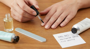 Applying cuticle oil to fingernails with a brush, alongside a handwritten note reading 'NAIL DO's: MOISTURIZE DAILY, FILE GENTLY.