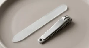 A sleek glass nail file and professional steel clippers on a clean surface for shaping nails correctly.