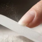 A macro photograph illustrating the singular directional filing technique. A close-up shows the edge of a medium-length natural nail.