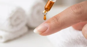 A close-up of amber cuticle oil being applied to a perfectly shaped natural nail for hydration.